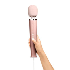 Hand holding Le Wand rose gold plug-in massager upright to show ergonomic handle size and grip