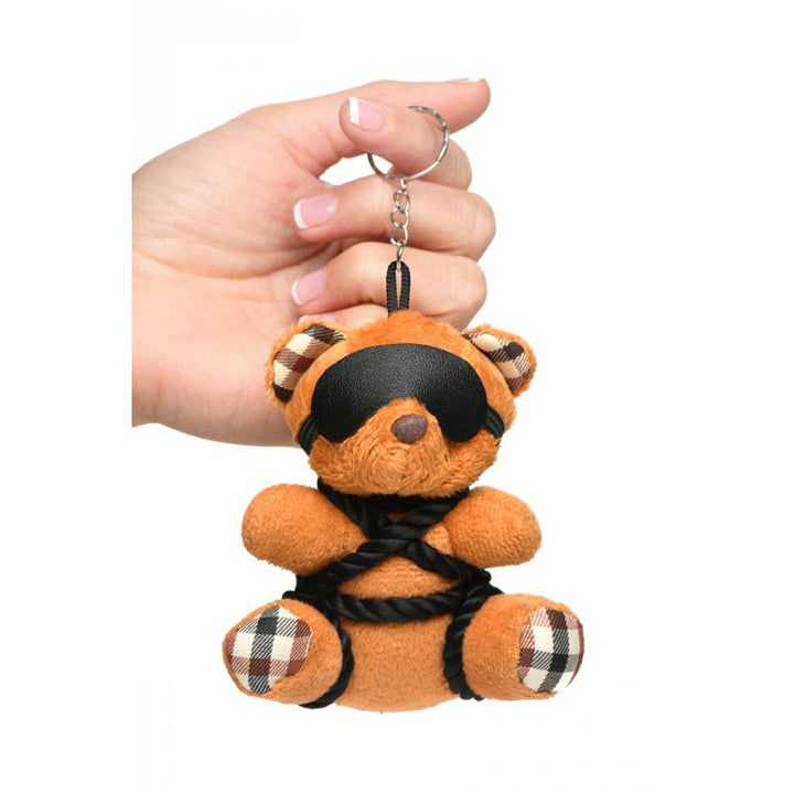 Hand holding Master Series Rope Bondage Teddy Bear Keychain with blindfold and black rope detail