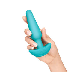 Hand holding medium teal silicone plug with b-Vibe logo on curved base, displaying slim ergonomic taper