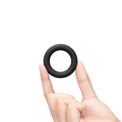 Hand holding one small black silicone cock ring showing compact size and smooth texture