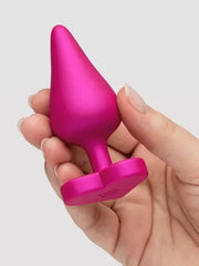 Hand holding pink ROMP Luster medium anal plug showing tapered tip and heart-shaped base