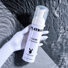 Hand holding Playboy Clean Foaming Toy Cleaner bottle over flowing water background
