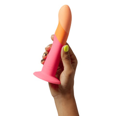 Hand holding ROMP Dizi dildo to show size scale, two-tone pink and orange finish
