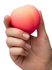 Hand holding the ROMP Pink Peach stimulator showing its compact peach-shaped silicone body