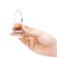Hand holding second-size clear glass plug upright, highlighting compact insertable length