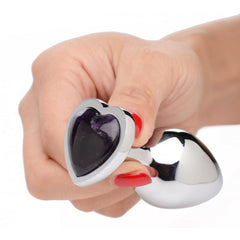 Hand holding a silver metal anal plug with a genuine amethyst heart gemstone at the base