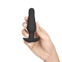 Hand holding small black silicone anal training plug showing smooth tapered tip and flared base for safe use