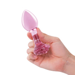 Hand holding a small pink glass plug upright, showing compact size and rose base grip