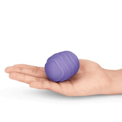 Hand holding a small purple ribbed silicone texture cover, showing compact palm-fitting size