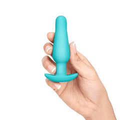 Hand holding small teal silicone plug from b-Vibe set, showing smooth tapered shape and flared base