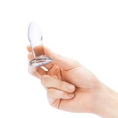 Hand holding smallest clear glass anal dilator, showing smooth tapered tip and flared base