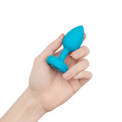Hand holding teal b-Vibe silicone jewel plug to show compact S/M size and smooth finish