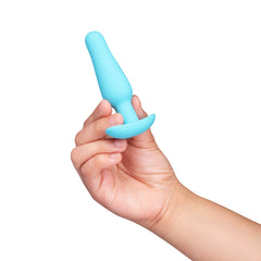 Hand holding teal tapered silicone anal plug by its flared base, showing beginner-friendly scale