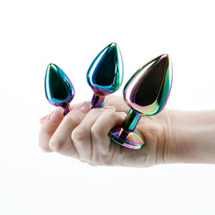 Hand holding three graduated multicolor metallic anal plugs showing relative size comparison
