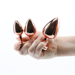 Hand holding three rose gold metal plugs from the Rear Assets kit, showing graduated sizes