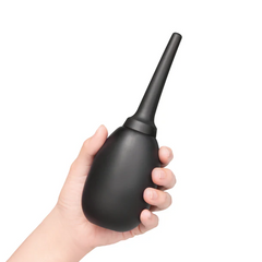 Hand holding upright black silicone anal douche, demonstrating compact travel-friendly size