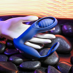 Hand holding the Zero Tolerance Extra Mile prostate massager above smooth dark stones