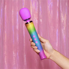 Hand displaying Le Wand Rainbow Ombre massager against shimmery pink backdrop