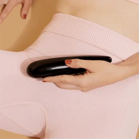 Hand pressing smooth black obsidian wand against hip area over blush-toned fabric