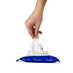 Hand pulling a single biodegradable wipe from open Dame Body Wipes blue resealable pack