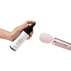 Hand spraying Le Wand toy cleaner onto pink silicone wand massager head