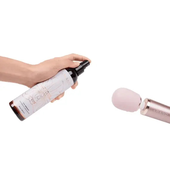 Hand spraying Le Wand Toy Cleaner toward pink silicone massager head for post-use care
