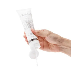 Hand squeezing Le Wand Coconut Love Oil tube, dispensing clear organic lubricant