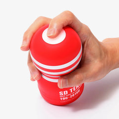 Hand squeezing the top dome of the red Tenga cup demonstrating its flexible soft outer body