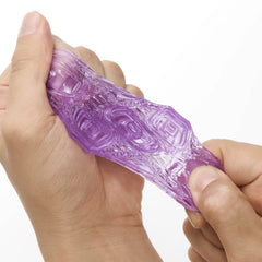Hands stretching a purple Tenga Uni gel massager, showing high-elasticity flexible material