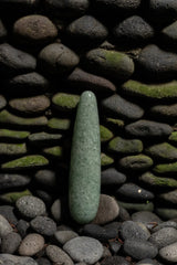 Indian Jade Original Wand standing upright among dark river stones, highlighting its deep green natural jade