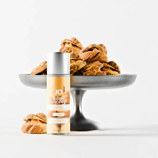 JO Bake Shoppe Orange Creampuff lubricant bottle displayed in front of pastries on a silver cake stand