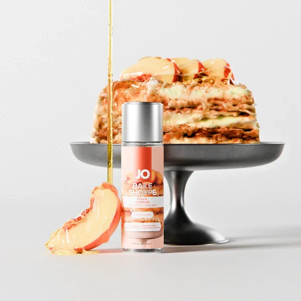 JO Bake Shoppe Peach Cobbler flavored lubricant bottle beside a layered peach cake on a cake stand