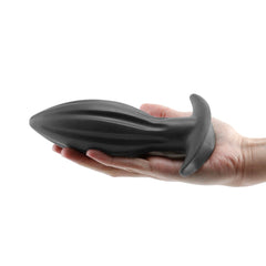 Large black silicone anal plug held in hand, showing full ribbed length and size reference