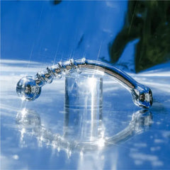 Le Wand Bow stainless steel dildo on reflective wet surface under running water showing waterproof design