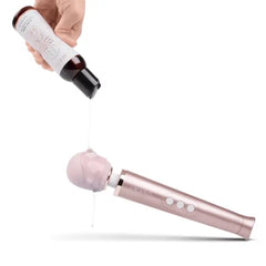 Le Wand lubricant being poured onto a rose gold wand massager head, showing ultra-thick gel texture