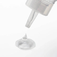 Close-up of lotion nozzle dispensing a small clear drop onto white surface, light viscosity