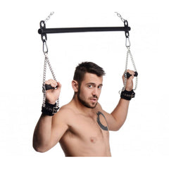 Male model holding chain wrist restraints attached to black steel Levitate Suspension Bar