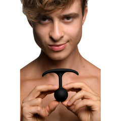 Man displaying black silicone weighted anal plug with curved T-bar base