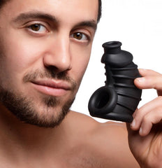Man holding Dark Chamber silicone chastity cage showing ribbed texture and dual openings