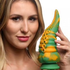Model holding Monstropus tentacled monster dildo showing green-yellow marbled silicone texture and scale