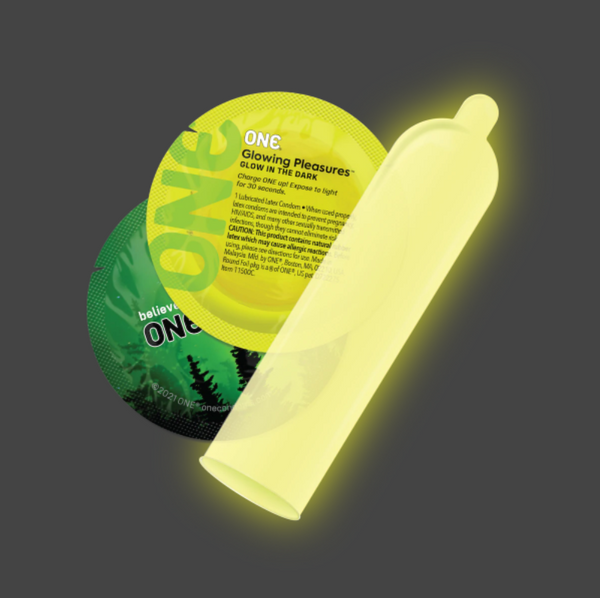 ONE Glowing Pleasures glow-in-the-dark condom beside its round foil packet, emitting bright yellow-green light