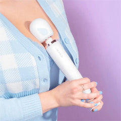Person in blue cardigan applying Le Wand massager head to upper arm for muscle relief