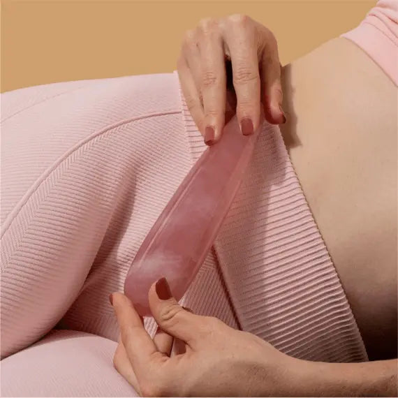 Person in pink activewear holding the rose quartz crystal wand against their hip and thigh