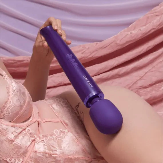 Person in pink lace resting Le Wand purple massager against thigh, showing real-world scale and use