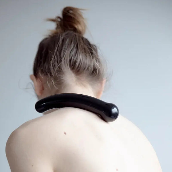 Person using the curved black crystal wand as a neck and shoulder massage tool, showing its ergonomic arc