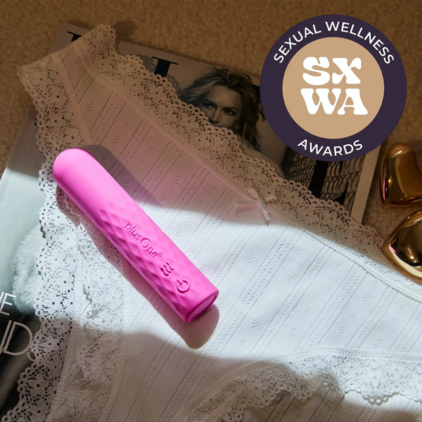 Pink plusOne super bullet resting on white lace fabric beside a magazine, Sexual Wellness Award badge shown