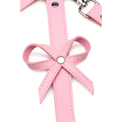 Close-up of pink vegan leather bow detail with stitching and silver snap hardware on harness strap