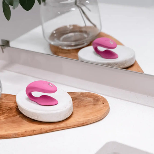 Pink We-Vibe Sync 2 couples vibrator resting on a marble dish atop a wooden tray near a mirror