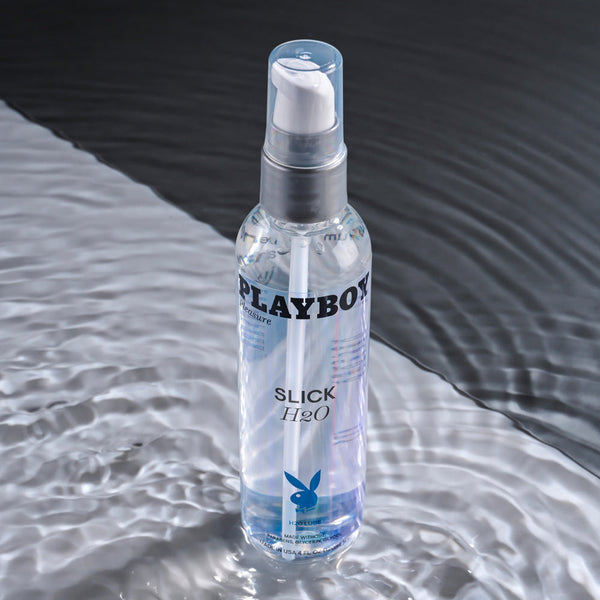Playboy Slick H2O 4oz bottle standing in shallow rippling water on grey surface