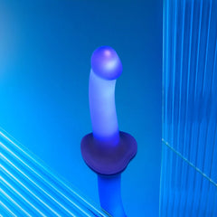 Purple silicone dildo glowing blue under LED lighting, mounted on suction base